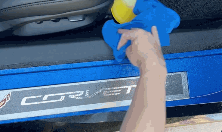 A hand wipes the interior door sill of a Corvette with a microfiber cloth and yellow applicator after a paint protection film installation.