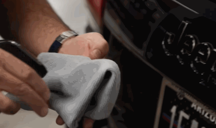 Close-up of a person spraying a solution onto a microfiber towel in preparation to apply ceramic coating to the front grille of a Jeep.