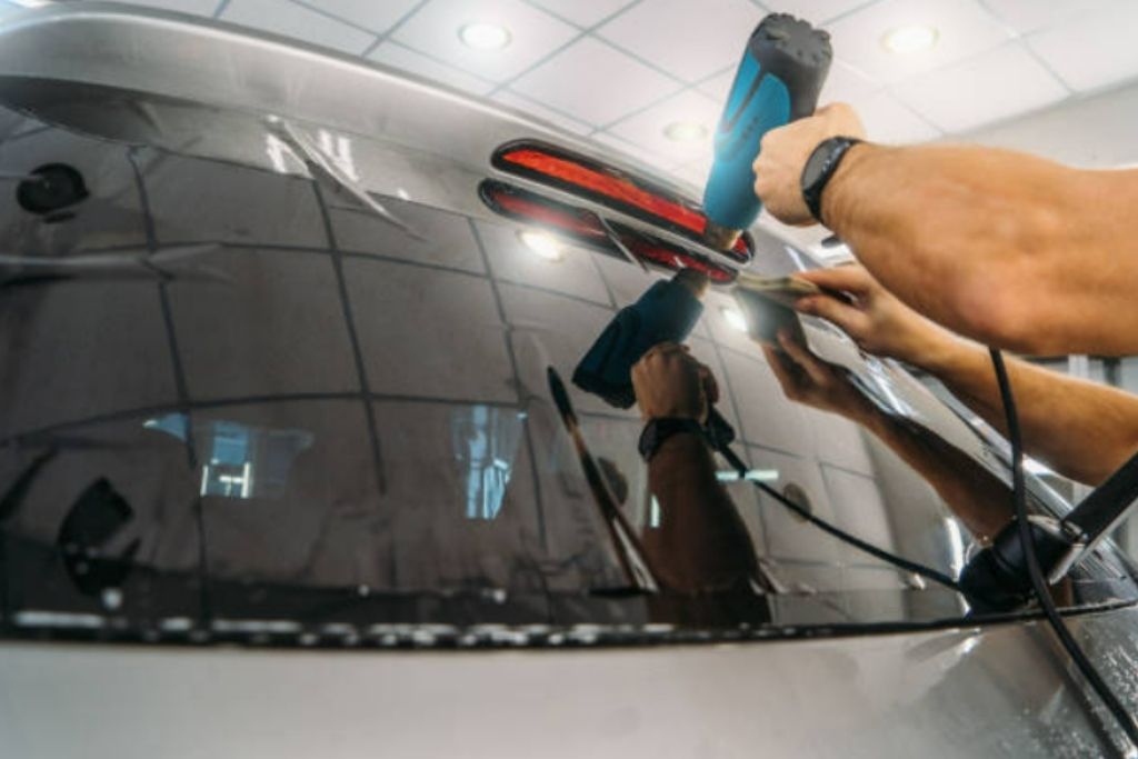 Technician using a heat gun to apply and shape window tint film on a vehicle’s rear window during professional installation.