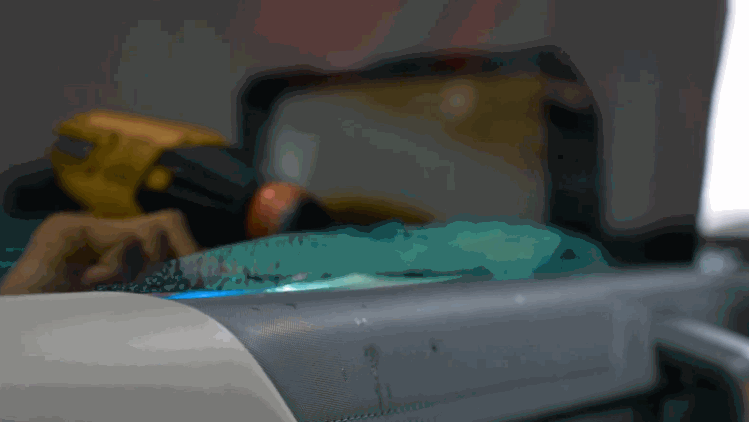 A technician uses a yellow heat gun on ceramic window tint inside a vehicle. The close up shows the film being shaped along the glass near the dashboard.
