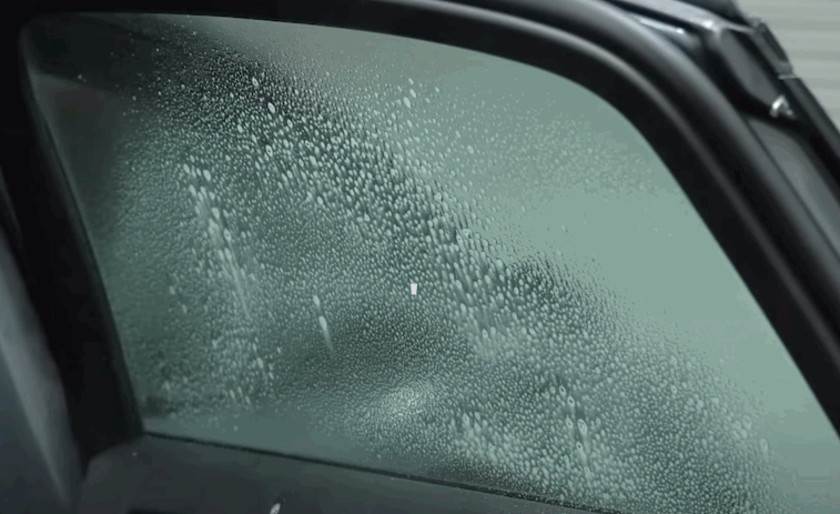 Close up of a side window covered with moisture droplets, showing Tesla window tint during installation or curing.