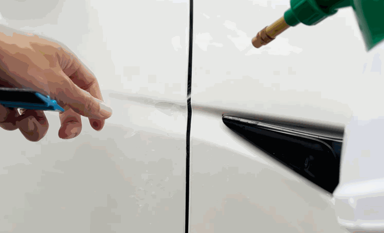 Close-up of an installer positioning paint protection film along the panel edge of a white car near a side trim piece.