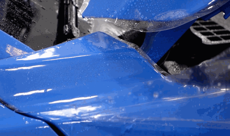 Paint protection film stretched across the curved front bumper of a blue car with moisture visible beneath the film.