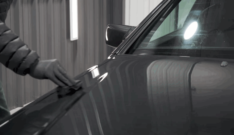 A technician wipes and inspects the glossy hood of a dark vehicle after surface treatment. This finishing step helps prepare or maintain a smooth surface when ceramic coating is used over paint protection film.